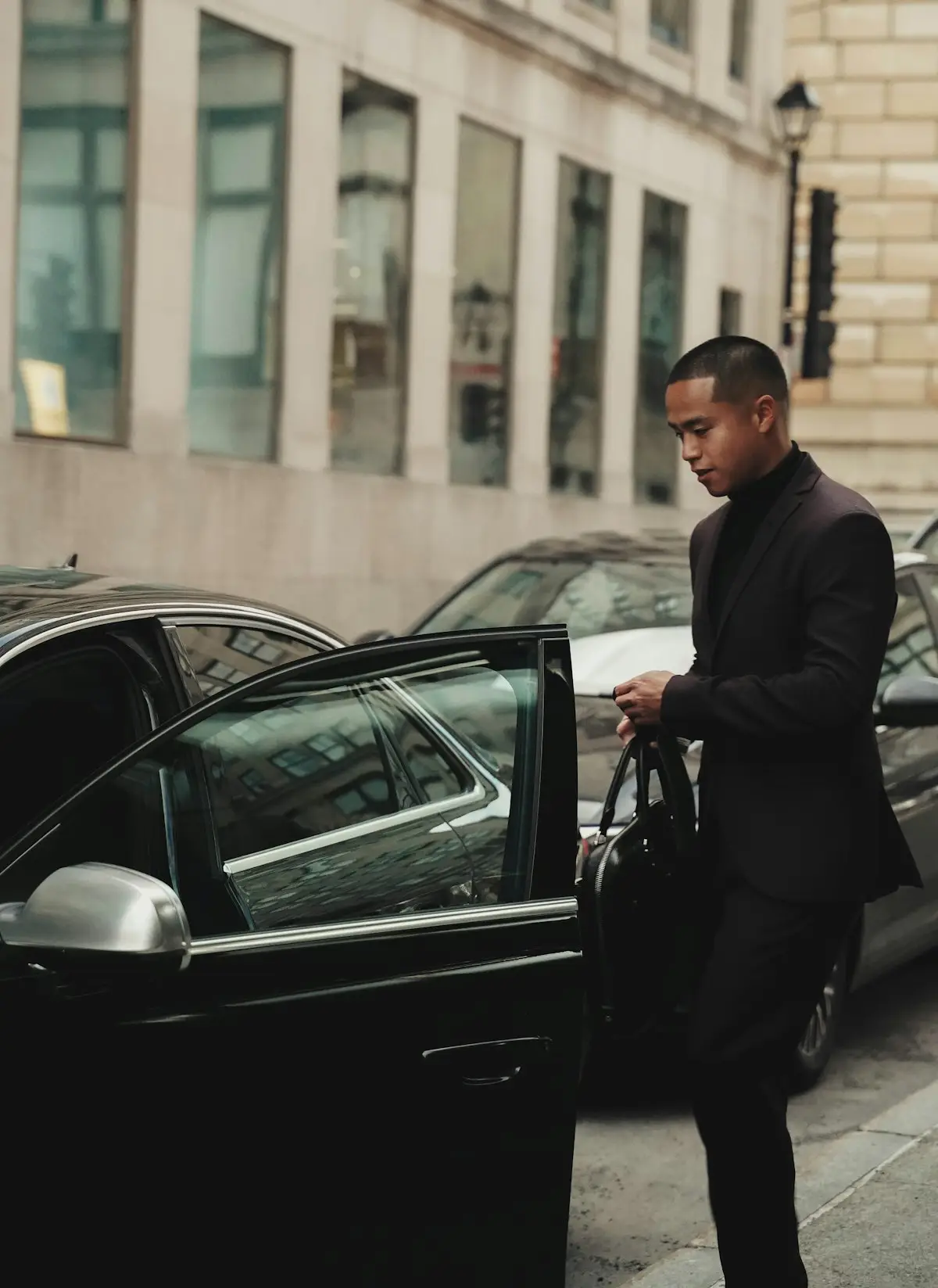 Chauffeur en costume devant une berline noire, immeuble haussmannien